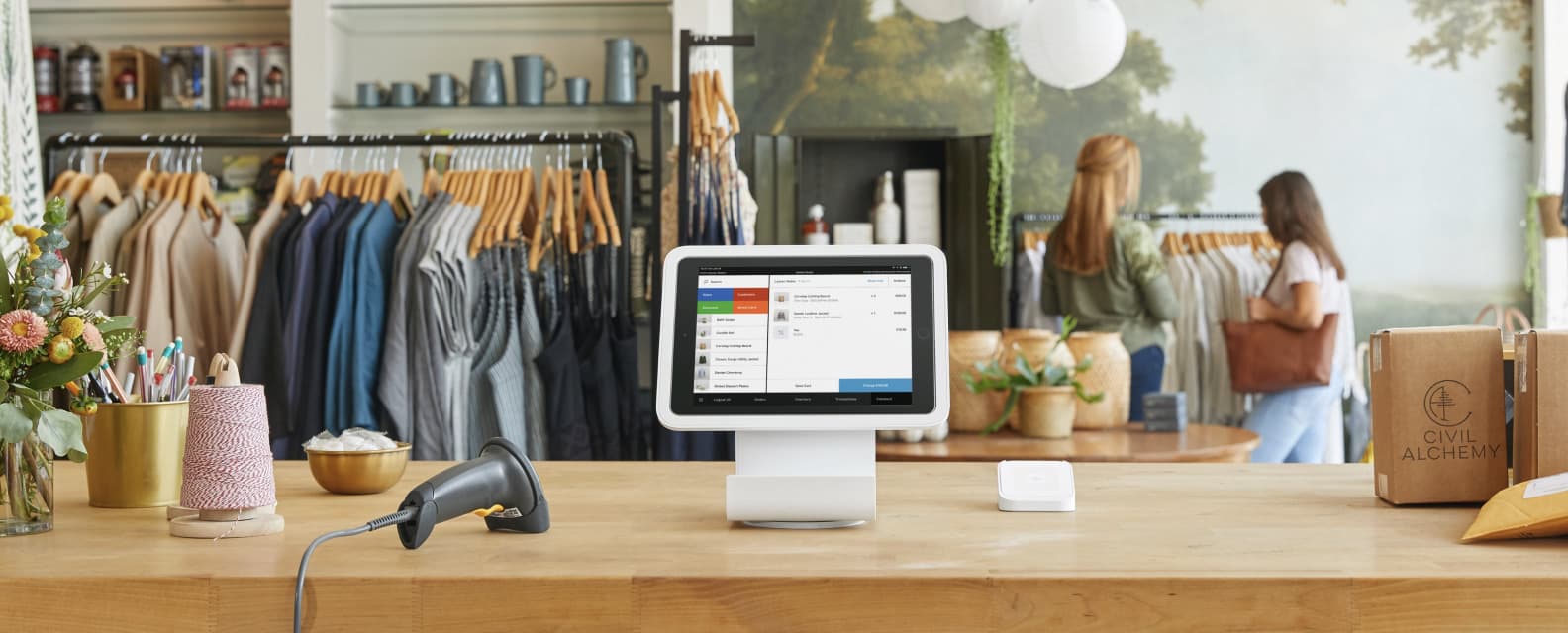 Square cash register sitting on a wood checkout counter in a clothing boutique